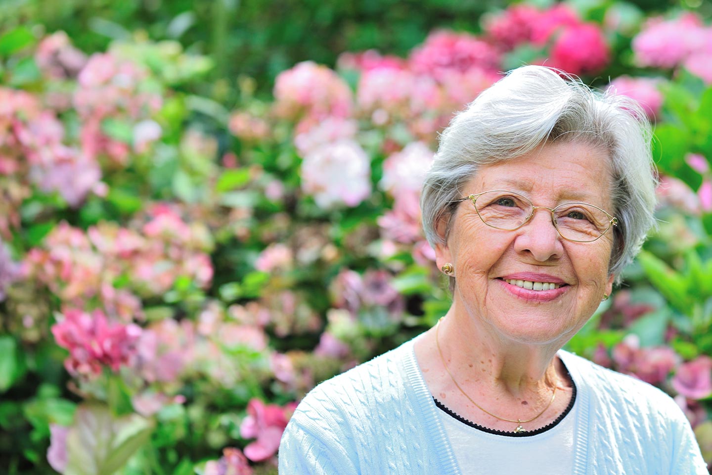 Image of an older woman outside in a garden full of flowers