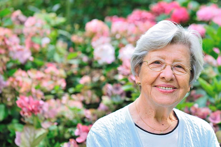 Bild einer älteren Frau draußen in einem Garten voller Blumen