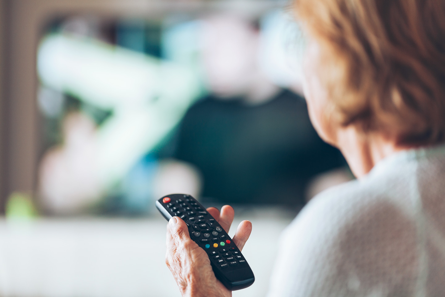 woman from behind holding remote control for television