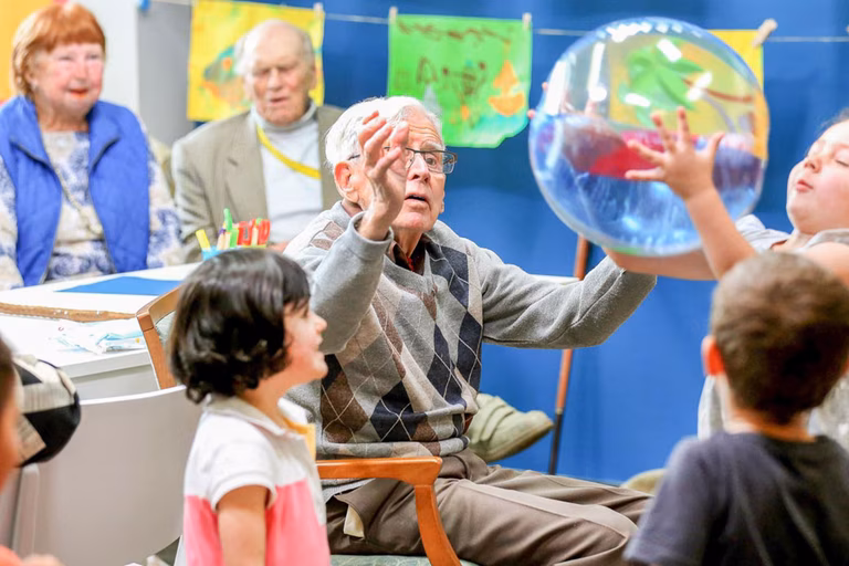 Image of an older man and primary children interacting at school