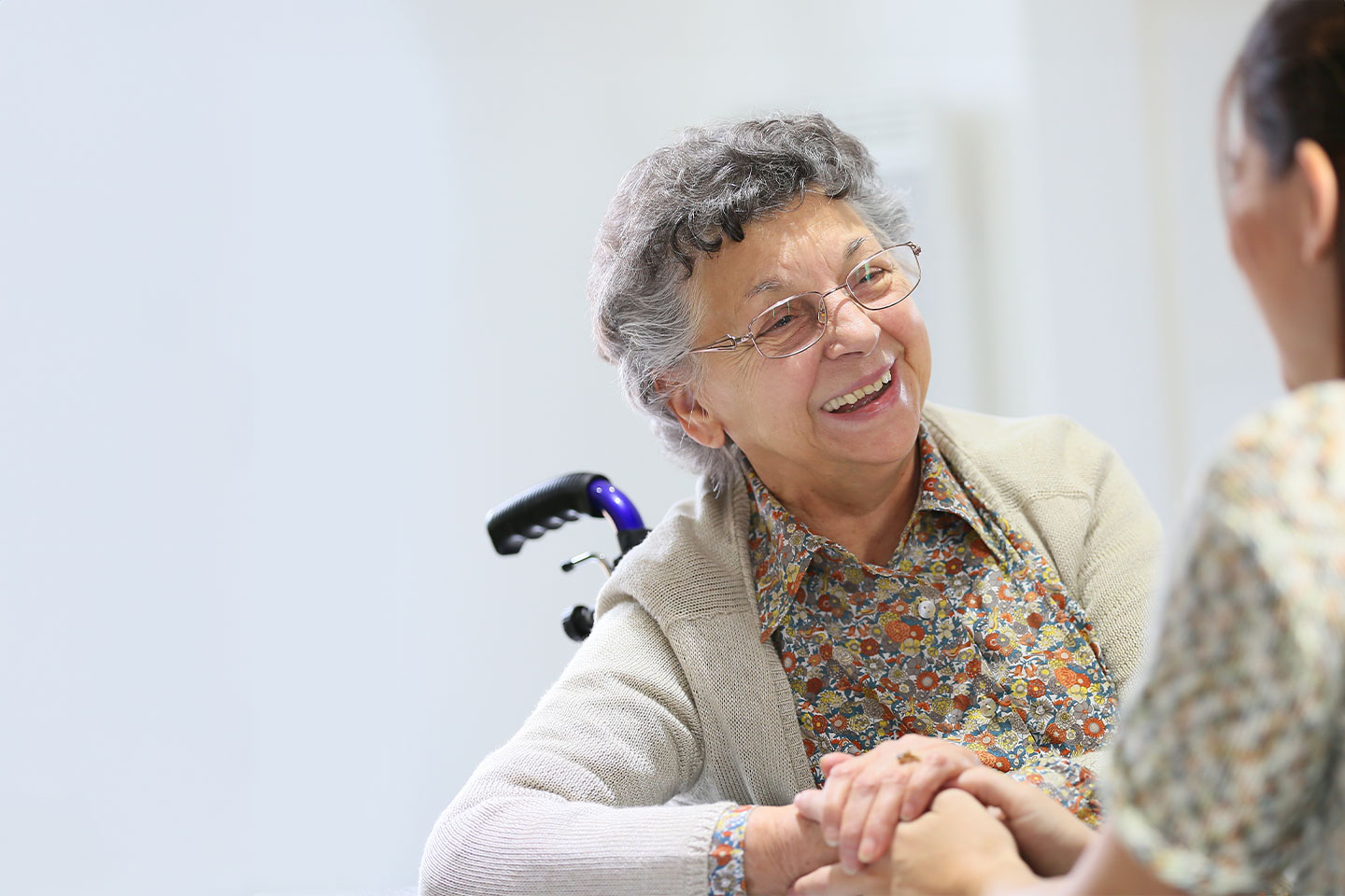 Smiling older woman in a wheelchair holding the hands of a carer