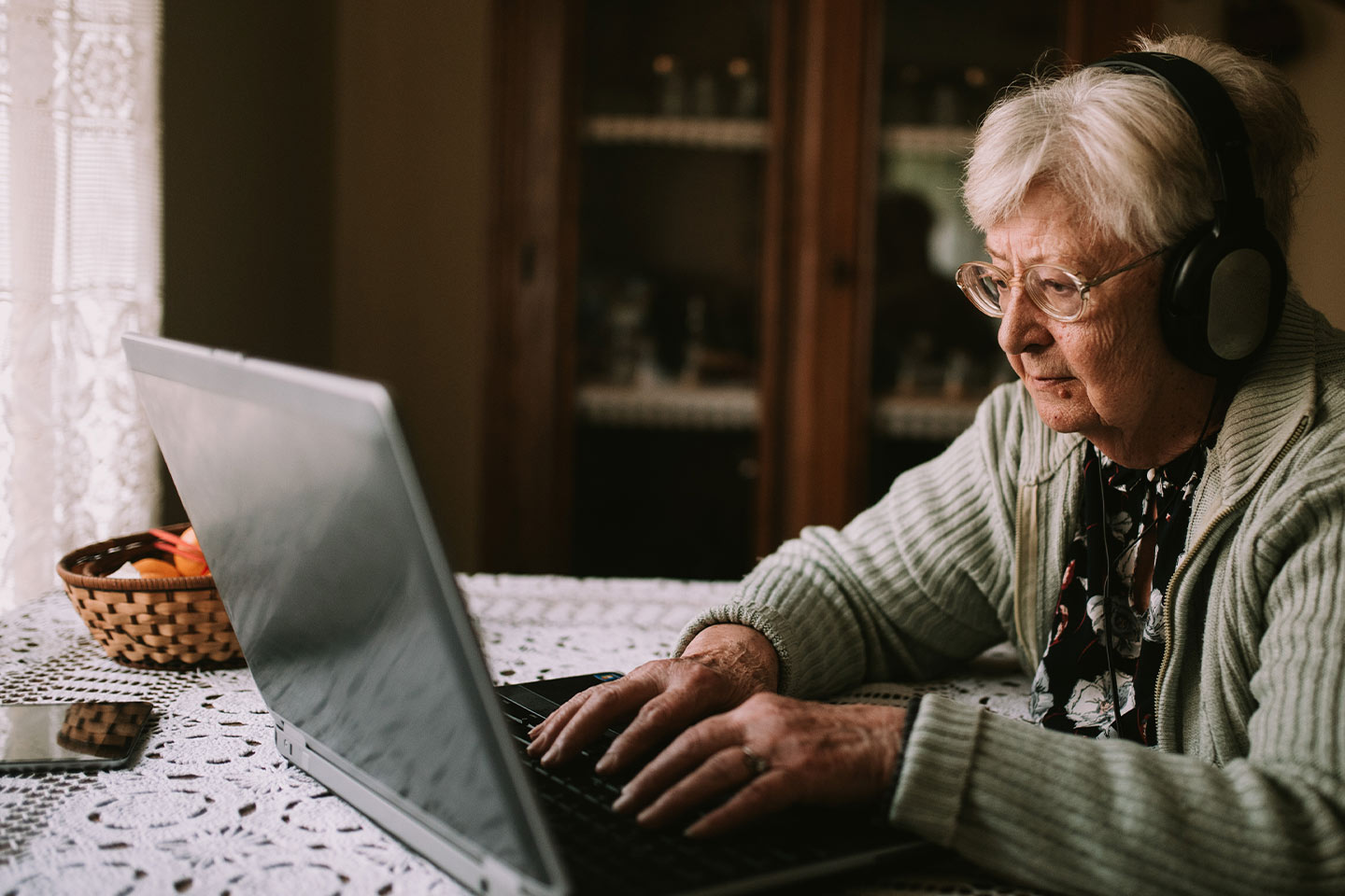 Photo of a woman sitting at a laptop wearing headphones
