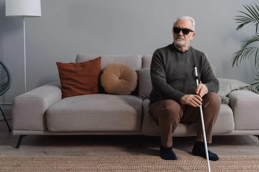 Photo of a man wearing black glasses and holding a white cane