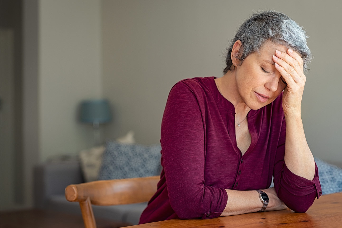 Photo of a woman in a maroon shirt with her head in her hands