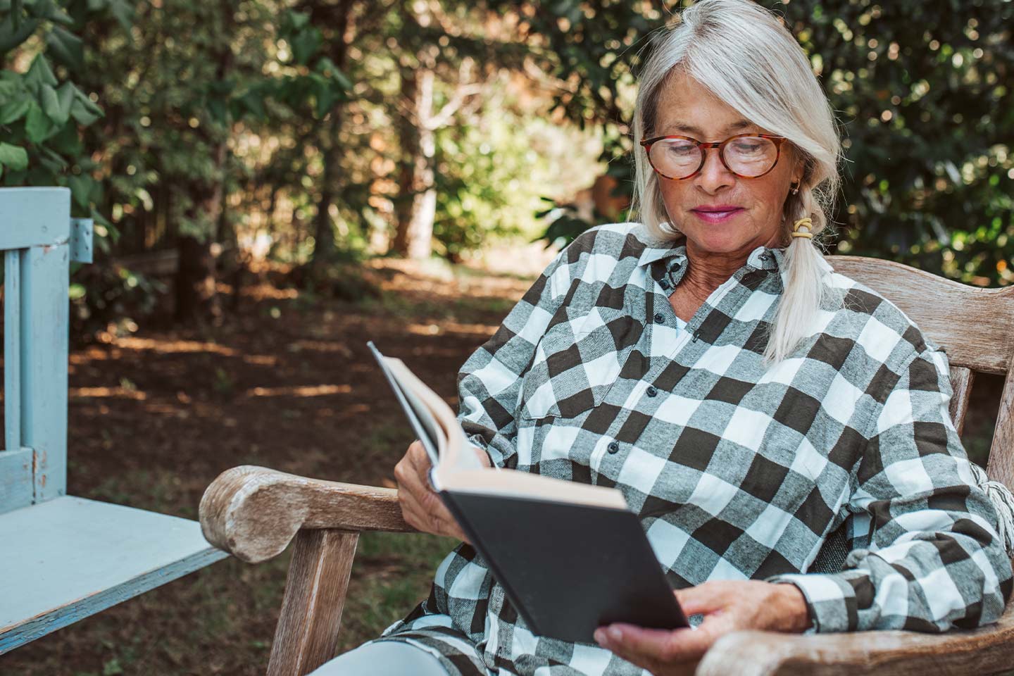Photo of woman with green checked shirt reading a book in a garden