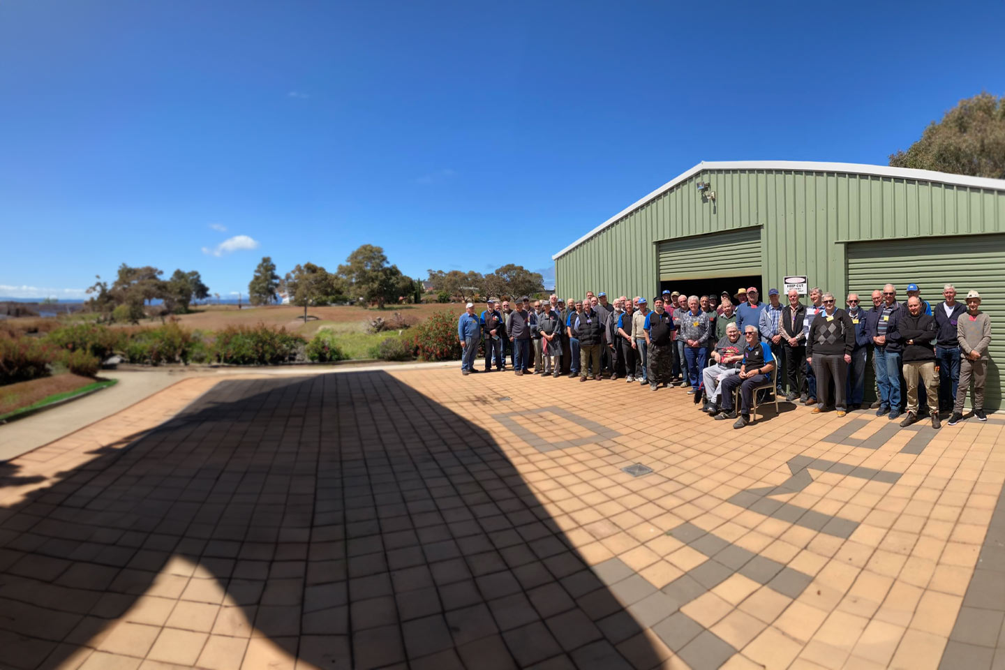 Photo of a group of men standing out the front of a large green shed