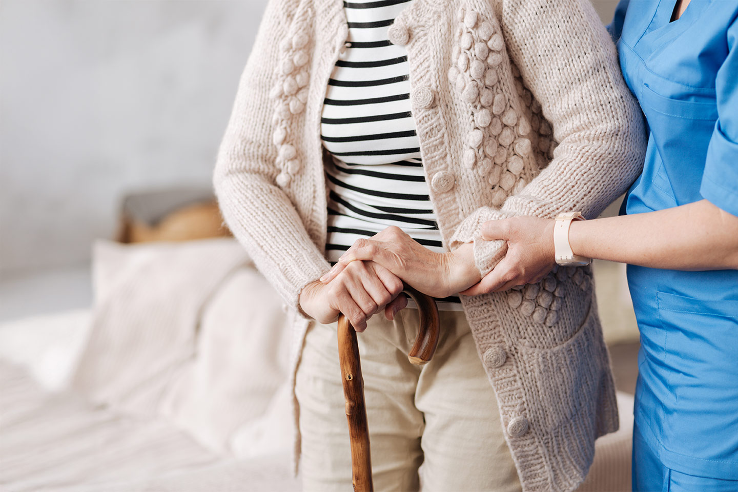 Photo of a person with a walking stick being helped by a health worker