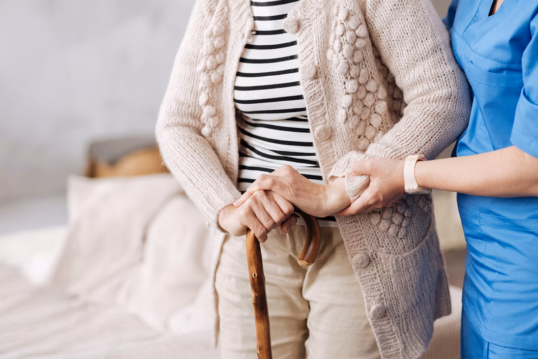 Photo of a person with a walking stick being helped by a health worker