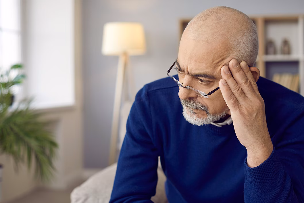 Photo of a man in a grey room resting his head on his fingertips