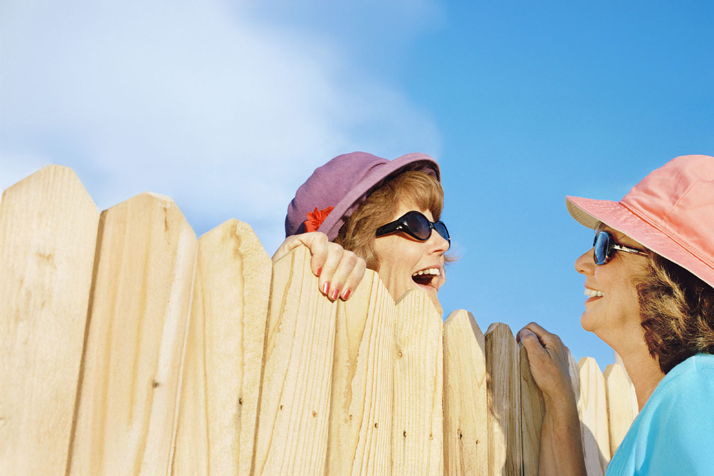Photo of two woman talking over a wooden picket fence