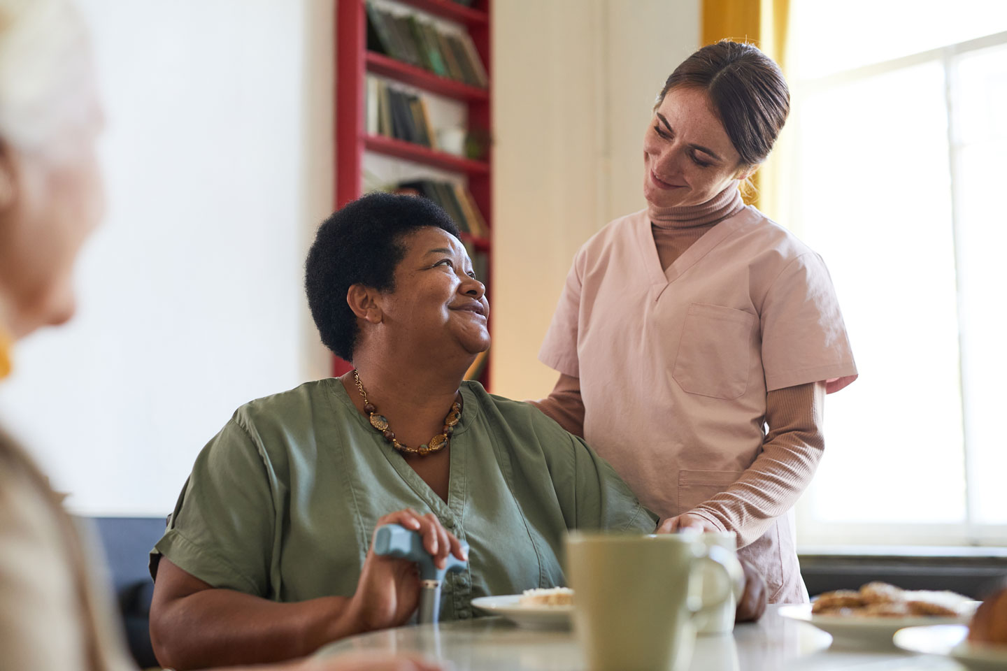 Portrait of smiling young woman assisting female patient during dinner at nursing home