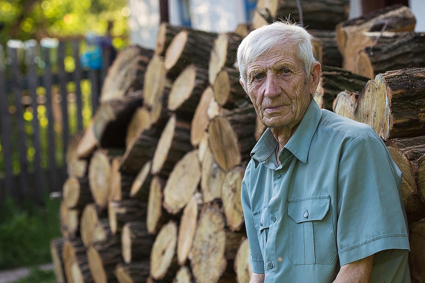 Photo of a man in a teal shirt in front of a log pile