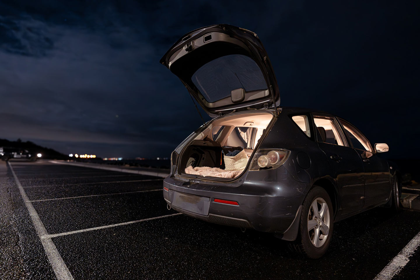 Photo of a car at night with a bed visible through the open rear hatch