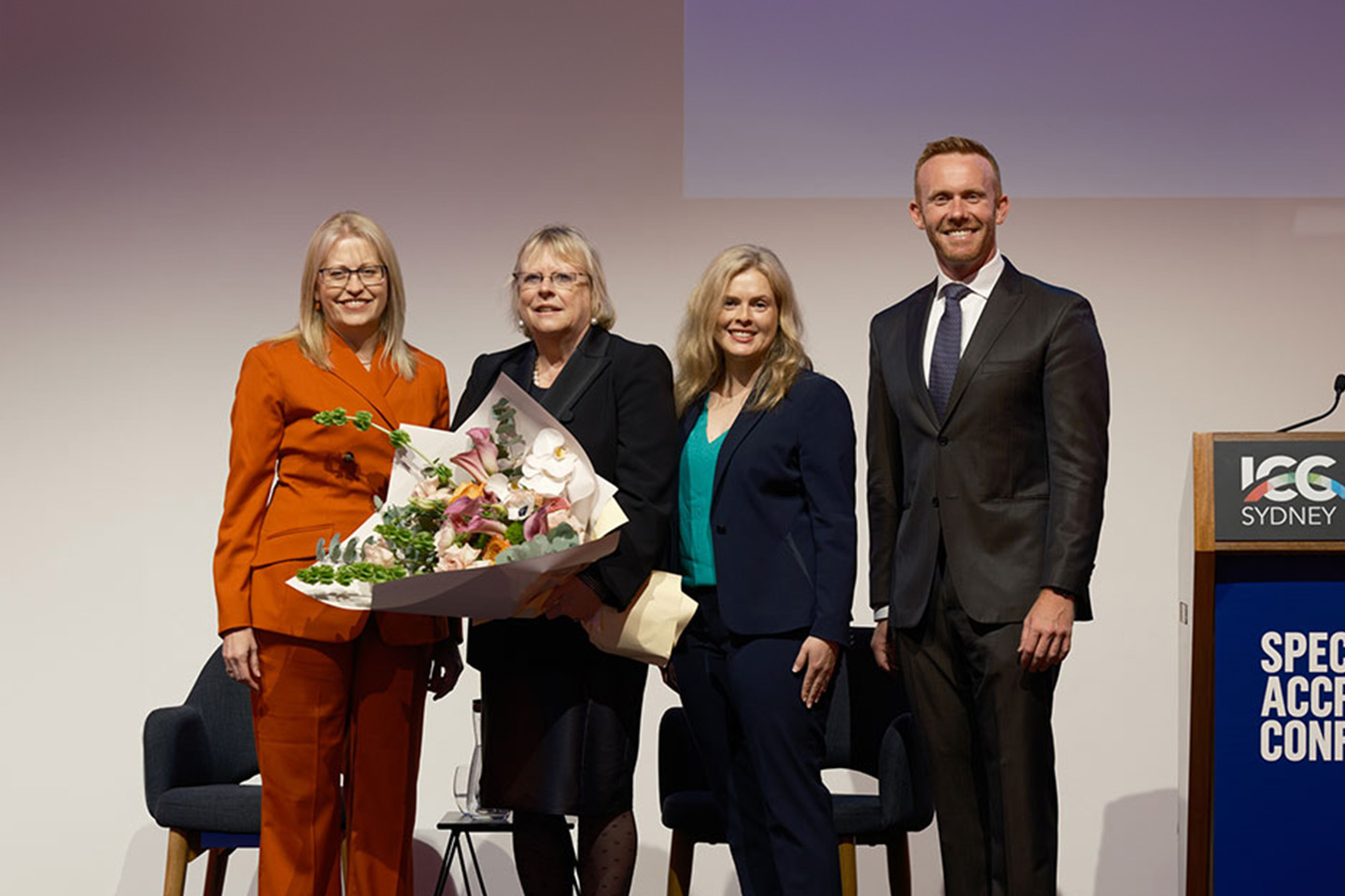 Photo of four lawyers on stage with a large bouquet