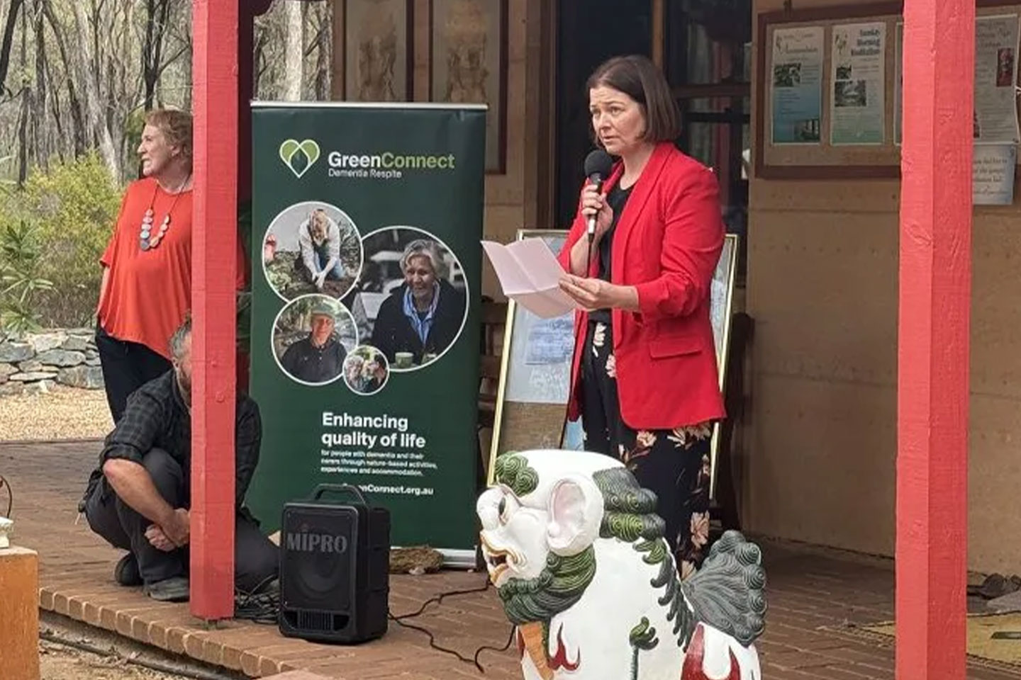 Photo of a woman in a red jacket speaking into a microphone