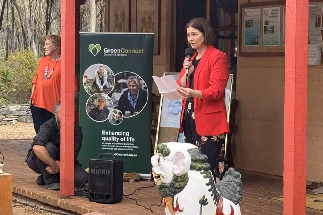 Photo of a woman in a red jacket speaking into a microphone