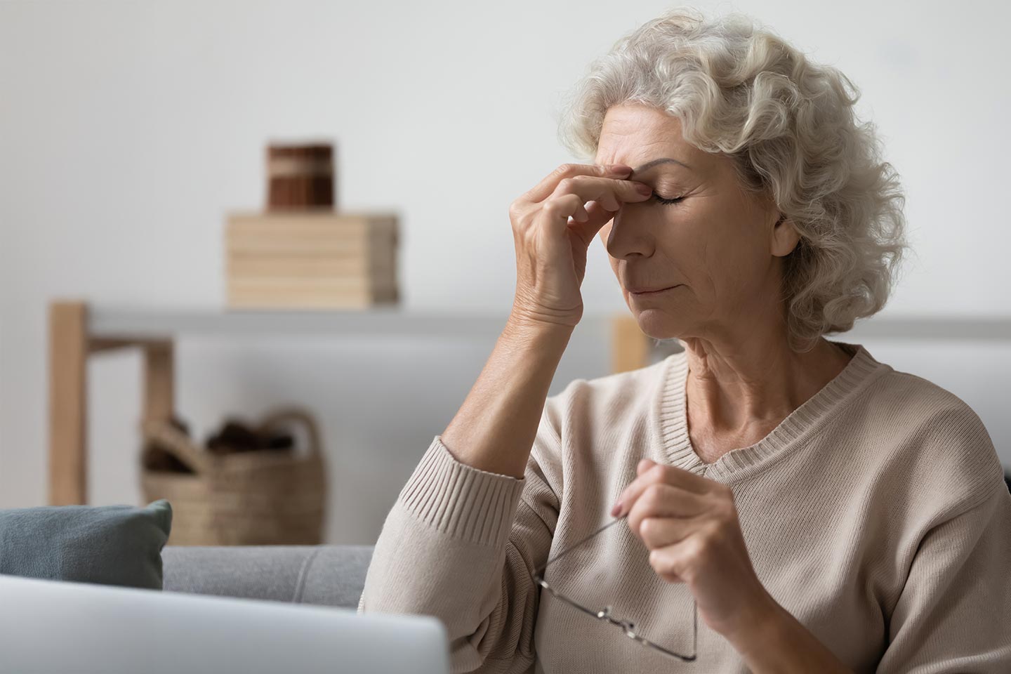 Woman in a beige jumper pinching the bridge of her nose
