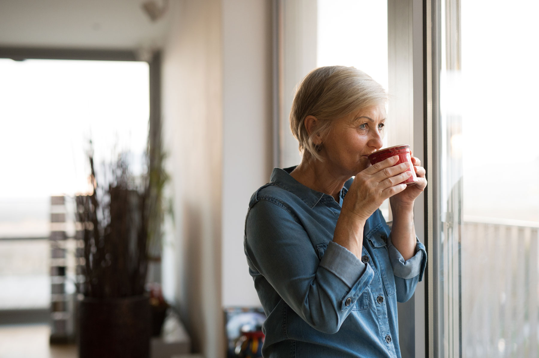Senior woman drinking from a mug and looking out of the window
