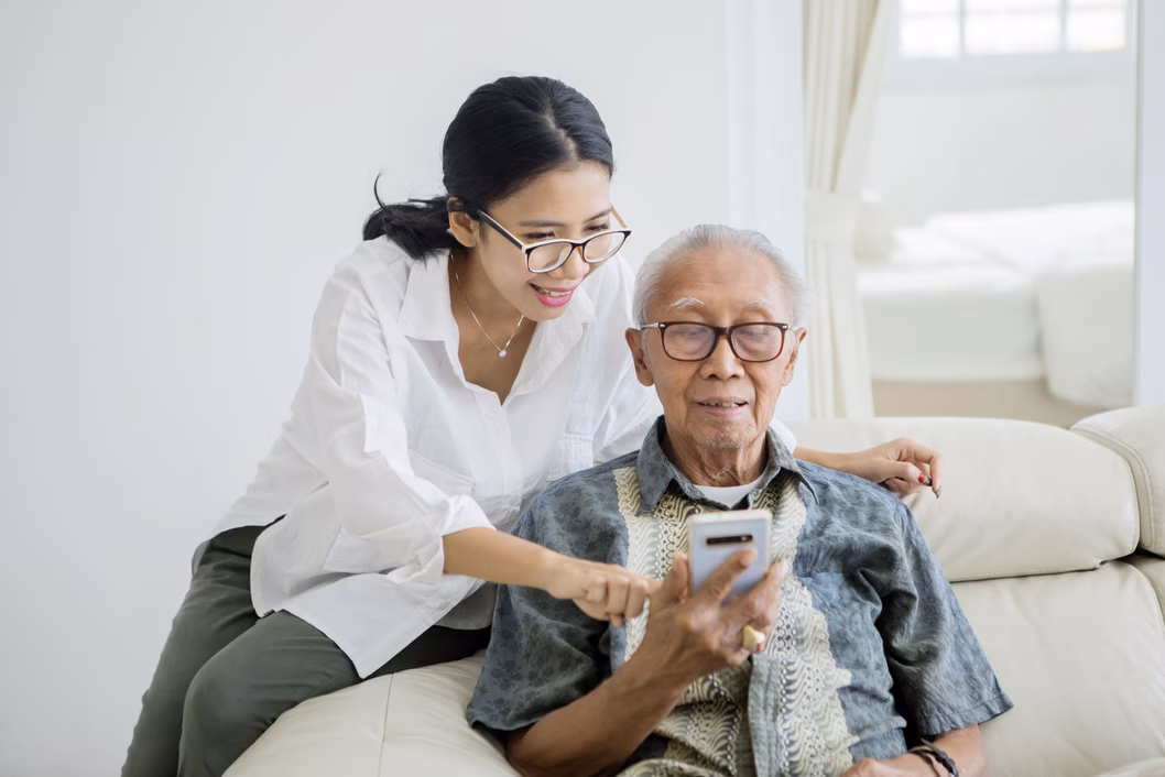 Carer helping senior man use mobile