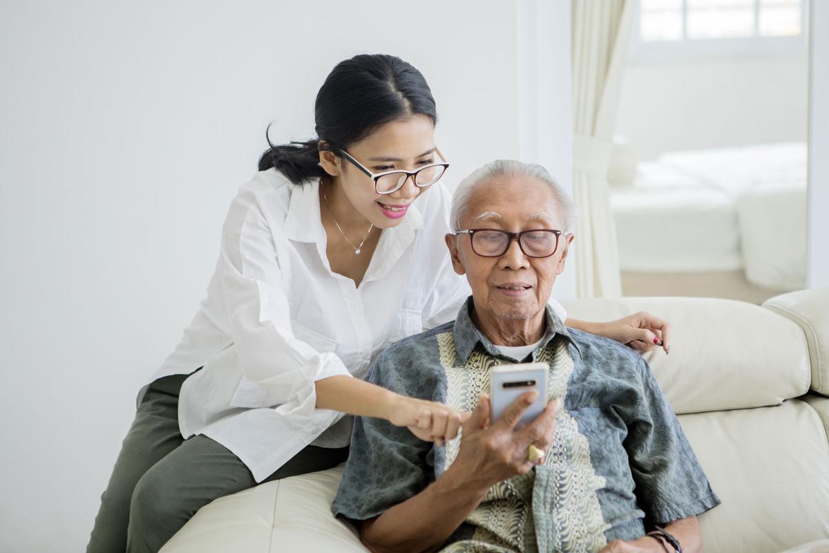 Carer helping senior man use mobile