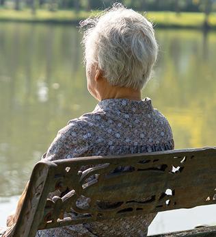 Photo of a person sitting on a park bench looking at a pond