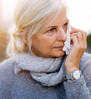 Photo of a woman in grey holding a tissue to her face