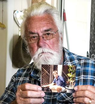 Photo of a white bearded man man holding up a photo
