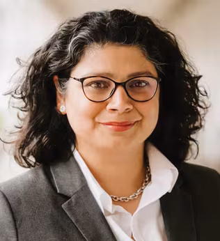 Photo of a smiling woman in a grey suit jacket and black glasses