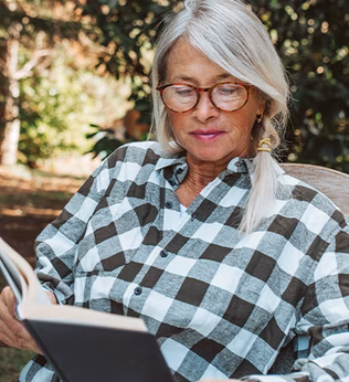 Photo of woman with green checked shirt reading a book in a garden