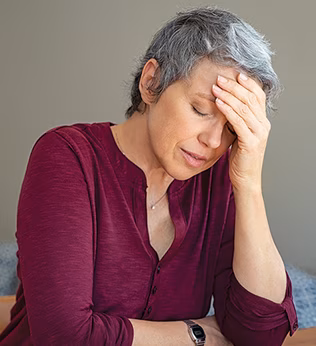 Photo of a woman in a maroon shirt with her head in her hands