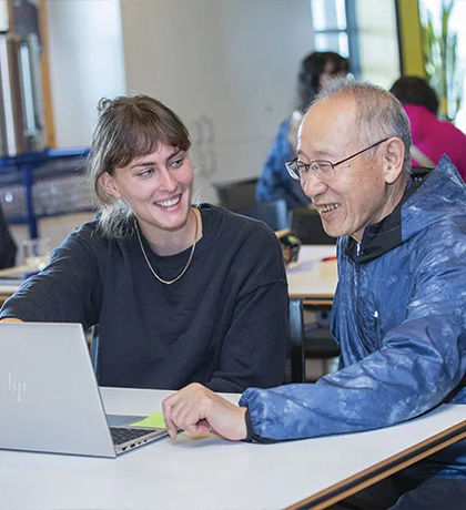 Photo of two people sitting at a laptop in a classroom