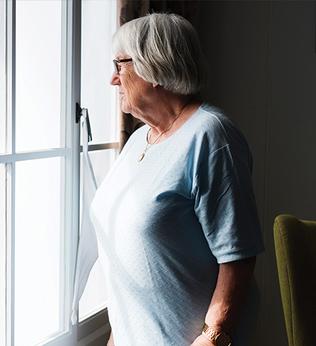 Photo of a woman in pale blue looking out of her window