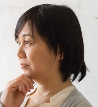 Photo of a woman in a grey cardigan with her hand on her chin