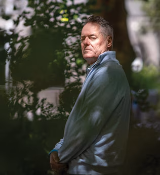 Photo of a man standing in dappled light in a garden