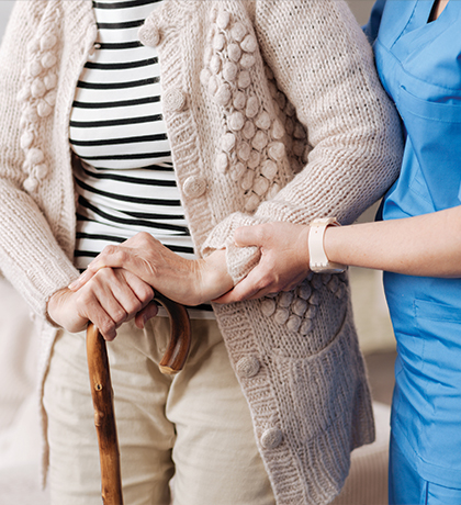 Photo of a person with a walking stick being helped by a health worker