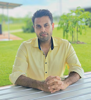 Photo of a man in a yellow shirt sitting at an outdoor table