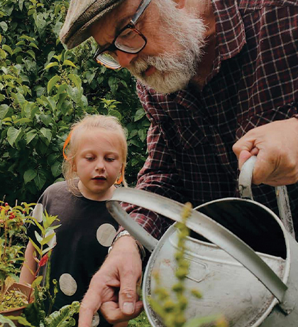 Photo in a garden of a curious child and a man with a watering can