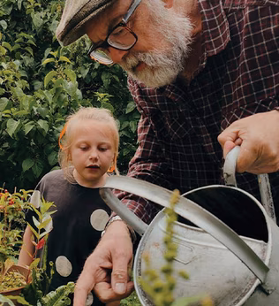Photo in a garden of a curious child and a man with a watering can
