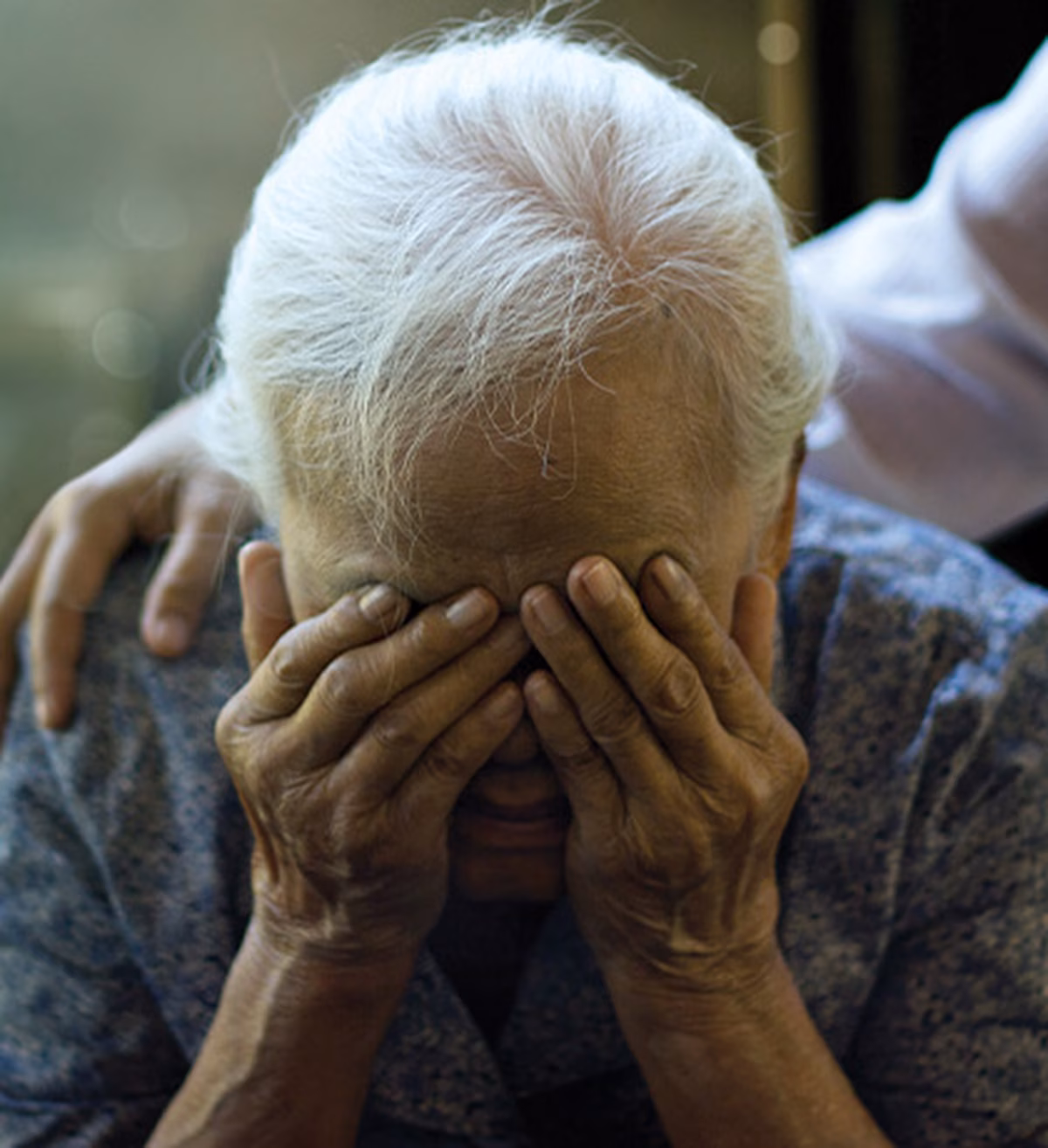 An older person crying with hands over their eyes