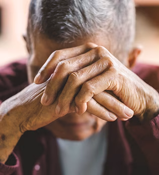 Photo of a man in a maroon shirt resting his head on his hands