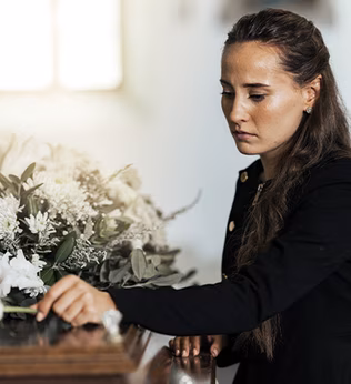 Photo of a woman placing a white rose on a coffin