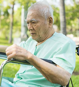 Photo of a man outdoors in a wheelchair wearing green hospital pyjamas