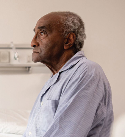 Photo of a man in blue pyjamas sitting on the edge of a hospital bed