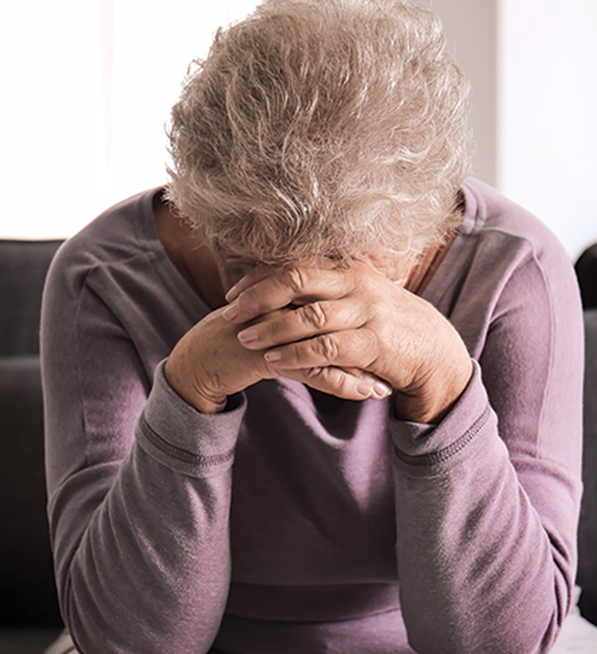 Photo of a woman in a lilac top resting her head on her hands