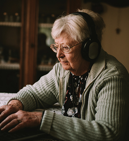 Photo of a woman sitting at a laptop wearing headphones