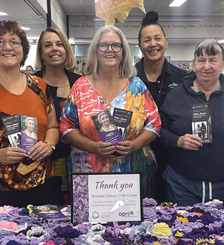 Photo of a group of smiling women standing behind a purple blanket