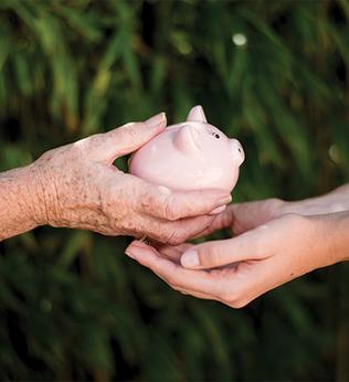 Photo of older hands giving piggy bank to younger hands