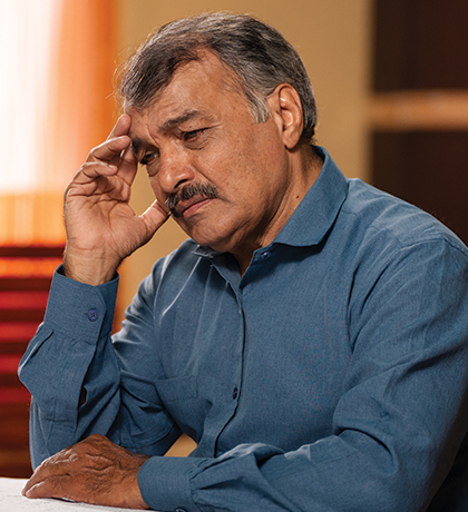 Photo of a seated man with his hand to his head