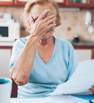 Photo of woman with hands over her eyes and paperwork in hand