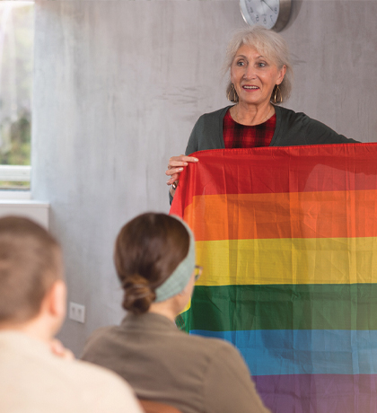 Photo of a speaker holding up a rainbow flag to her audience